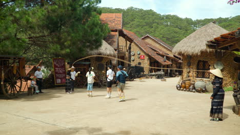 Group-of-Korean-Travelers-Jump-Over-Rope-at-Cu-Lan-Ethnic-Village-Street-in-Da-Lat-City,-Vietnam---slow-motion