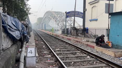 Toma-Cinematográfica-De-Una-Línea-Ferroviaria-Vacía-Al-Lado-De-Un-Puente-Peatonal-Y-Un-Hombre-Rompiendo-Carbones-Durante-La-Mañana-En-Calcuta,-India