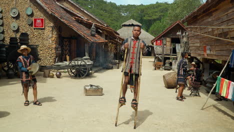 Artistas-Con-Ropa-Tradicional-Tocan-Tambores-Y-Caminan-Sobre-Zancos-En-La-Antigua-Calle-Del-Pueblo-étnico-Cu-Lan-En-La-Ciudad-De-Da-Lat,-Vietnam,-Recorrido-Cultural-étnico-Vietnamita---Cámara-Lenta