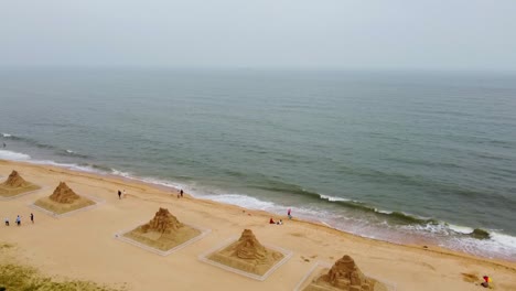 Vista-Aérea-De-La-Playa-Con-Plataforma-Rodante,-Volando-Sobre-Varias-Esculturas-De-Arena,-Día-Brumoso-En-Nanhai,-China