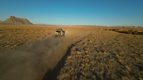 Aufregender-FPV-Drohnenflug-Verfolgt-Einen-Weißen-Geländewagen,-Der-Auf-Einer-Staubigen-Wüstenstraße-In-Richtung-Factory-Butte,-Utah,-Fährt