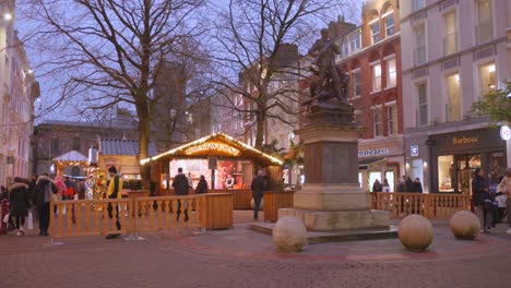 Turistas-Paseando-Por-El-Mercado-Navideño-Durante-La-Noche-Con-Un-Lindo-Puesto-De-Venta