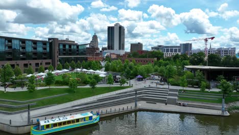 Colorful-riverboat-on-water-near-a-park-with-urban-backdrop-in-Fort-Wayne,-Indiana