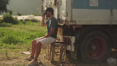 Ein-Junger-Mann-Sitzt-Auf-Einer-Abgenutzten-Holzbank-Hinter-Einem-Sattelschlepper-Und-Hält-Eine-Vintage-Kamera-Ins-Gesicht