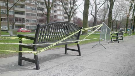 Park-Benches-With-Yellow-Barrier-Tape-Across-Them-In-Local-Green-Space-In-Montreal