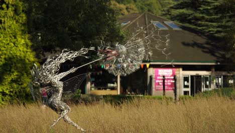 Die-Drahtfee-Mit-Einem-Löwenzahn-Dreht-Sich-Langsam-Im-Wind-Auf-Der-Wiese-Am-Haupteingang-Der-Trentham-Estate-Gardens