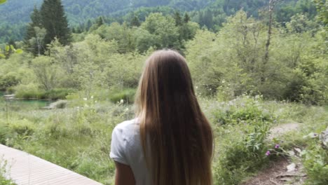 Yung-sporty-girl-walking-on-a-wooden-deck-to-a-small-emerald-lake