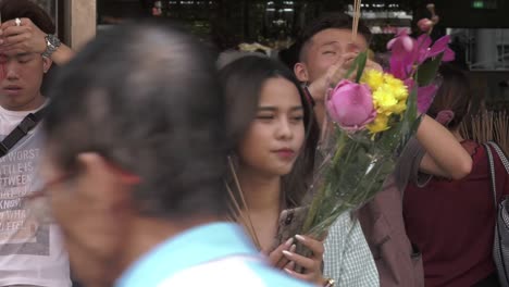 Young-Woman-with-smartphone-burning-incense-sticks-while-praying-among-other-devotees,-in-Singapore---Medium-static-shot