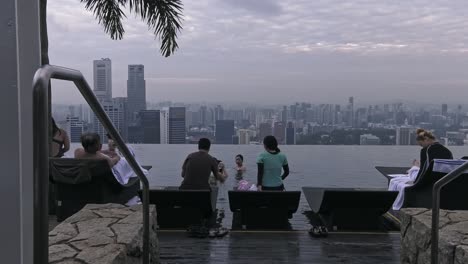 Turistas-Relajándose-En-Tumbonas-Cerca-De-La-Piscina-Infinita-De-La-Azotea-Del-Skypark-Del-Hotel-Marina-Bay-Sands,-En-Singapur---Toma-Estática-De-Ancho-Medio