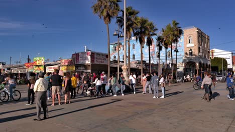 Personas-Que-Usan-Máscaras-Y-Se-Reúnen-Al-Aire-Libre-Para-Ver-Un-Espectáculo-En-El-Paseo-Marítimo-De-Venice-Beach-Durante-La-Pandemia-De-Covid-19-En-Los-Ángeles,-California,-EE.UU.