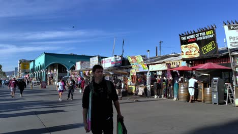 Tourists-eating-and-shopping-around-at-the-Famous-Venice-Beach-Boardwalk,-sunny-morning,-in-Los-Angeles,-California,-USA---pan-view