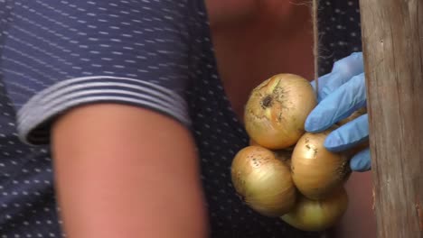 Persona-Agregando-Cebollas-Doradas-A-Una-Cuerda-Para-Crear-Un-Manojo-En-El-Mercado