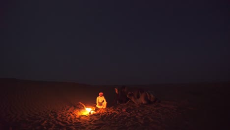 Anochecer-En-El-Sombrío-Desierto-De-Omán-Iluminado-Por-Una-Fogata-De-Un-Hombre-Con-Una-Caravana-De-Camellos---Amplia-Toma-Estática