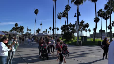 Acera-Ocupada-Con-Gente-Con-Máscaras,-Caminando-Y-Andando-En-Bicicleta-En-La-Entrada-Del-Paseo-Marítimo-De-Venice-Beach-En-Los-ángeles,-California,-Estados-Unidos-Durante-La-Pandemia-De-Covid-19