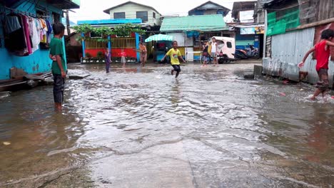 Children-make-a-makeshift-skim-board-from-from-old-plywood-during-monsoon-season,-Philippines