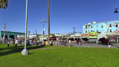 Venice-Beach-Boardwalk-with-people-walking-around-and-shopping-with-artwork-painted-on-building-in-the-background-in-Los-Angeles,-California,-USA