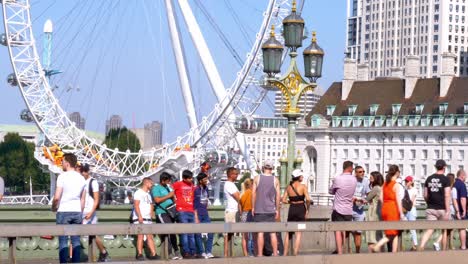 Toma-Estática-De-Turistas-Cruzando-El-Puente-De-Westminster-Con-La-Rueda-Del-Milenio-Del-London-Eye-Como-Telón-De-Fondo