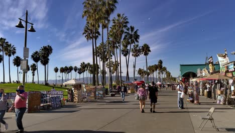 People-walking-along-the-Venice-Beach-Boardwalk-with-shopping-stalls-on-both-sides-during-the-Covid-19-pandemic-on-a-sunny-day-in-Los-Angeles,-California,-USA