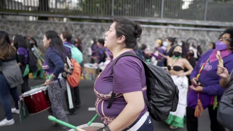 A-woman-wearing-a-purple-shirt-is-playing-the-drums-with-more-women-during-the-protest-in-the-International-Women's-day-in-Quito,-Ecuador