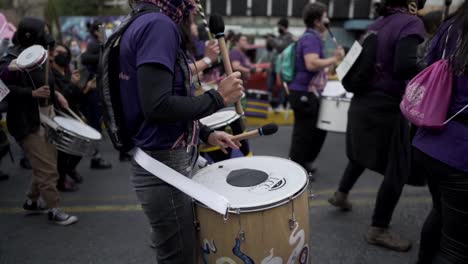 Varias-Mujeres-Vestidas-De-Morado-Tocan-Tambores-Mientras-Marchan-Durante-La-Protesta-En-El-Día-Internacional-De-La-Mujer-En-Quito,-Ecuador