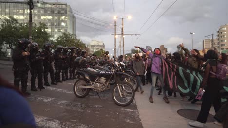 A-group-of-women-jump-and-sing-to-police-officers-while-holding-up-sings-of-protest-during-the-International-Women's-day-in-Quito,-Ecuador