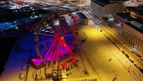 Aerial-view-in-front-of-red-illuminated-skywheel,-revealing-the-market-square-and-the-Helsinki-cathedral,-winter-night-in-Finland---tilt,-drone-shot