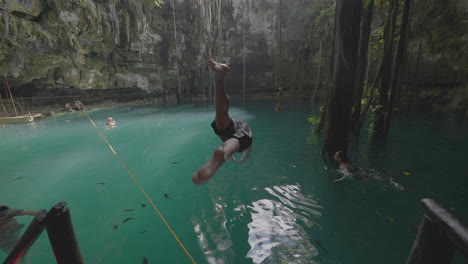 Parte-Posterior-De-Un-Hombre-Saltando-Desde-Una-Plataforma-Al-Agua-Turquesa-De-Un-Cenote-Mexicano,-Cámara-Lenta-A-Pantalla-Completa