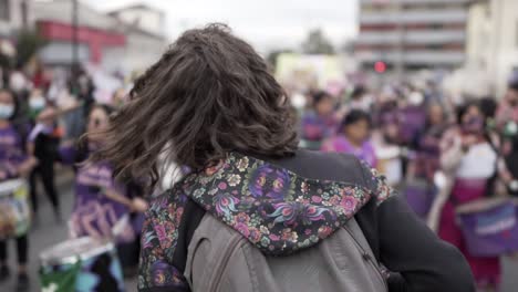 A-woman-is-smiling-and-dancing-as-she-leads-a-group-of-women-dressed-in-purple-who-are-playing-drums-as-they-march-during-the-protest-in-the-International-Women's-day-in-Quito,-Ecuador