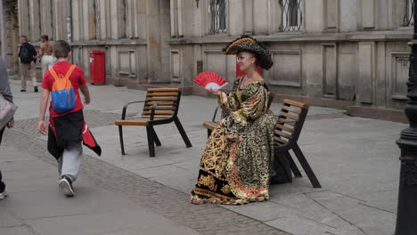 Woman-with-old-medieval-dress-on-bench-with-hand-fan