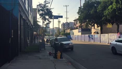 Gente-Caminando-Por-Las-Aceras-A-Lo-Largo-De-La-Calle-Con-Autos-Estacionados-Y-Tráfico-En-El-Distrito-De-Las-Artes-De-Los-Ángeles