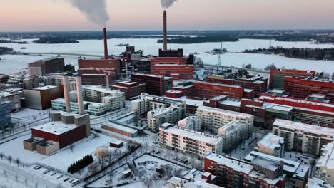 Vista-Aérea-De-Chimeneas-Humeantes,-Puesta-De-Sol-De-Invierno-En-Helsinki,-Finlandia---Seguimiento,-Disparo-De-Drone