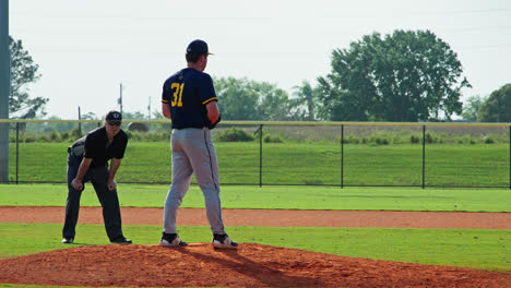 Pitcher-On-Mound-Throws-Baseball-With-An-Umpire-Standing-Behind-Him-During-A-Baseball-Game