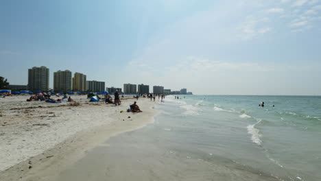 Menschen,-Die-Am-Strand-Entlang-Spazieren-Und-Spaß-Beim-Schwimmen-Im-Meer-Haben,-Am-Clearwater-Beach-Mit-Hotels-Im-Hintergrund,-Florida