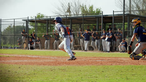 Baseball-Player-Swings-And-Hits-The-Baseball-and-Runs-For-First-Base-As-His-Team-Watches-from-The-Dugout-Behind-Him