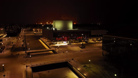 Vista-Aérea-Ascendente-Frente-Al-Teatro-Iluminado-De-Oulu,-Noche-De-Invierno-En-Finlandia