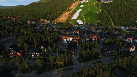 Vista-Aérea-Sobre-Edificios-Iluminados-Por-El-Sol-Y-Laderas-De-Levi,-Tarde-De-Verano-En-Laponia,-Finlandia---Rotación,-Retroceso,-Disparo-Con-Drones