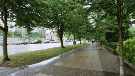 Person-With-Umbrella-Walking-Under-The-Rain-On-Paved-Sidewalk-In-Vancouver,-Canada