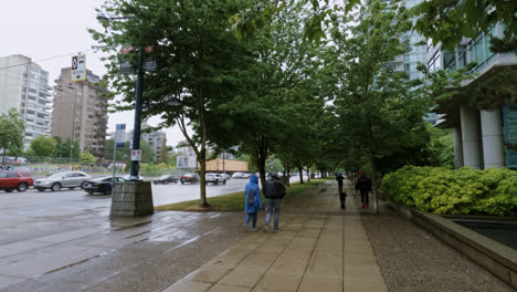 People-Walking-In-The-Rain-with-Umbrellas-and-Raincoats-On-Paved-Sidewalk-In-Vancouver,-Canada