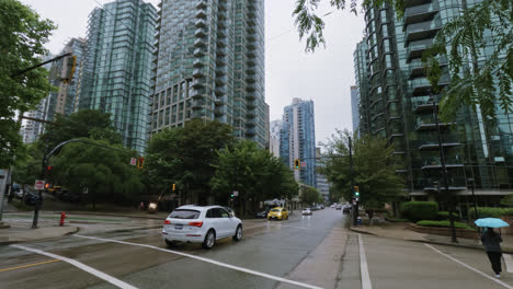 Autos-Fahren-Auf-Den-Nassen-Asphaltstraßen-Der-Innenstadt-Von-Vancouver,-Kanada,-Während-Menschen-Mit-Regenschirmen-Vorbeigehen,-Totale