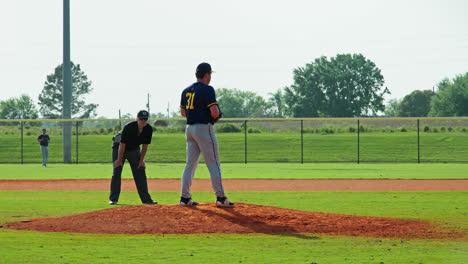 Pitcher-On-Mound-Throws-The-Baseball-With-An-Umpire-Behind-Him-During-Baseball-Tournament