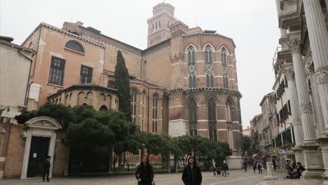 Vista-De-La-Calle-De-La-Basílica-De-Santa-María-Gloriosa-Dei-Frari,-Gente-Caminando,-Algunos-Con-Máscaras-Y-Disfraces-De-Carnaval,-Algunos-Con-Máscaras-Protectoras