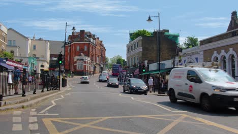 London-Bus-Driving-Through-Blackheath-Village-High-Street-on-Warm-Summer-Day