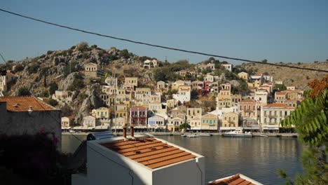 Vista-De-Los-Coloridos-Edificios-En-La-Colina-De-Ano-Symi-Junto-Al-Puerto,-Casas-Y-Cables-Eléctricos-En-Primer-Plano