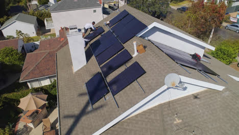 órbita-Aérea-Lenta-Alrededor-De-Tres-Trabajadores-En-La-Azotea-Instalando-Y-Realizando-Mantenimiento-En-Múltiples-Paneles-Solares-En-Un-Día-Soleado-En-Los-ángeles,-California---órbita,-Disparo-De-Drones