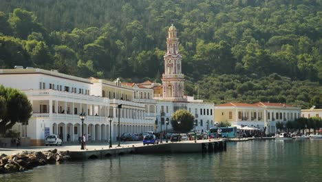 The-harbour-of-Panormitis-with-the-monastery-of-Archangel-Michael,-Forest-and-trees-on-hill-in-background