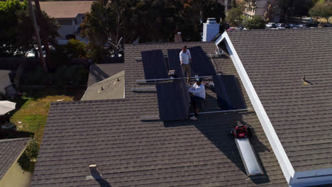 órbita-Aérea-Alrededor-Del-Frente-De-La-Azotea-De-Una-Casa-Con-Trabajadores-Instalando-Y-Realizando-Mantenimiento-En-Múltiples-Paneles-Solares-En-Los-ángeles,-California---Disparo-De-Drones