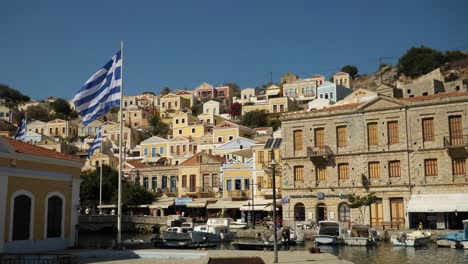 Bunte-Häuser-Von-Ano-Symi-Und-Griechische-Flaggen-Wehen-Im-Wind-Im-Hafen