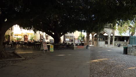 Fast-Leeres-Restaurant-Auf-Dem-Platz-Der-Altstadt-Von-Rhodos-Im-Schatten-Großer-Bäume