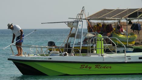 Man-on-a-green-boat-looking-for-something-in-the-water-at-Kolymbia-Harbour