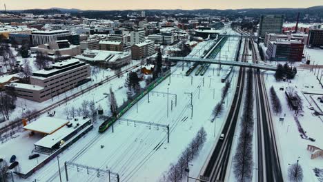 Luftaufnahme-Eines-Zuges,-Der-Einen-Verschneiten-Bahnhof-In-Jyväskylä,-Finnland,-Verlässt-–-Rückwärtsgang,-Drohnenaufnahme